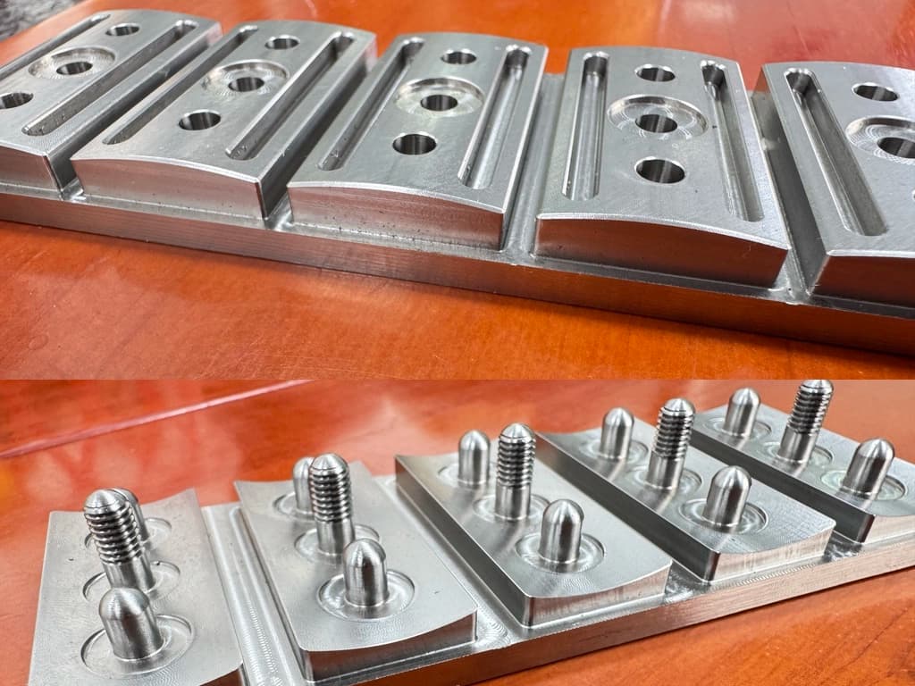 Perspective photo of five Vector safety razor heads mid-process, showing CNC-machined cap pins and base plate bevels still attached to the bar-stock fixture before the second machining pass