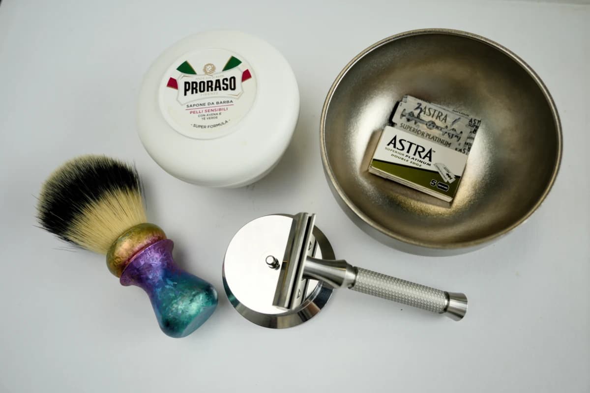 Astra Superior Platinum green DE blade pack and the ORMIXA Vector 316L safety razor with a Proraso soap, titanium bowl and gradient brush on a neutral surface