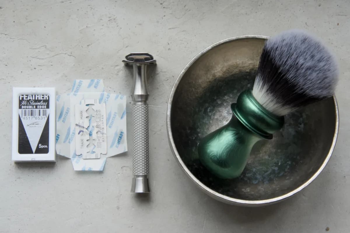 Feather Hi-Stainless blade, wrapper and five-blade case beside the ORMIXA Vector 316L razor, titanium bowl and synthetic brush