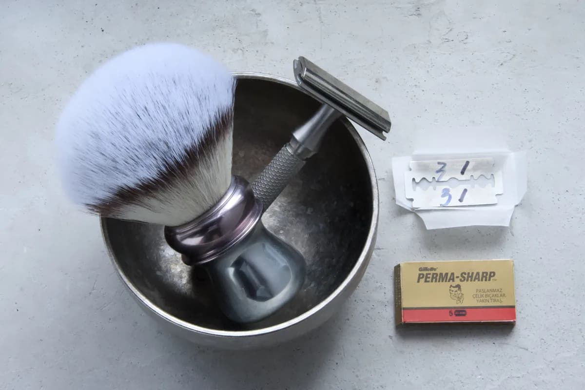 Gillette Perma-Sharp 5-pack, used blades on wax paper, the ORMIXA Vector 316L safety razor, a titanium bowl and an ORMIXA Harbor synthetic brush on a concrete surface