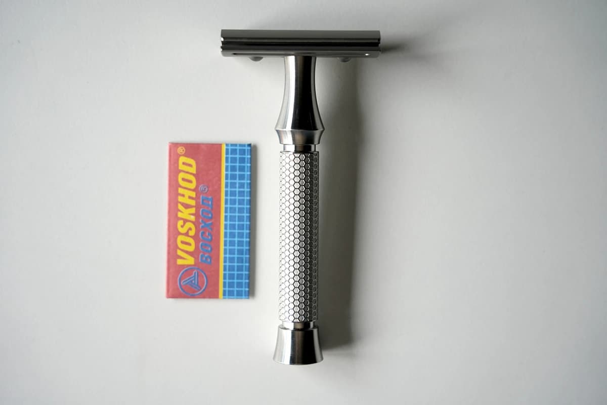 Voskhod Teflon Coated DE blade pack next to the ORMIXA Vector TC4 titanium safety razor on a neutral surface
